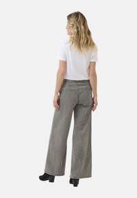 Pantalone širokog kroja sa prugicama u sivoj i bijeloj boji, s visokim strukom i stražnjim džepovima. U kombinaciji s jednostavnom bijelom majicom kratkih rukava.