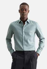 Lichtblauw button-up shirt met een spread collar, lange mouwen en witte knopen, gecombineerd met donkerblauwe broek. Glad stof met een subtiele glans.