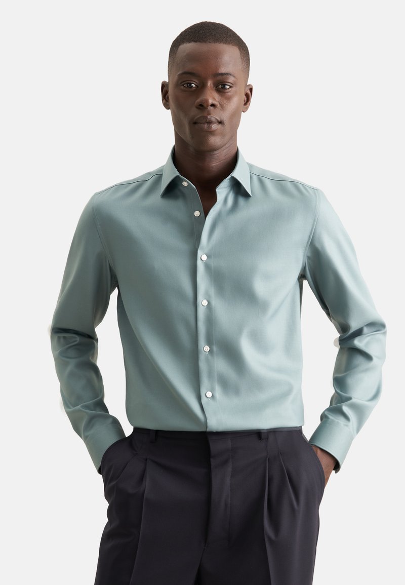 Lichtblauw button-up shirt met een spread collar, lange mouwen en witte knopen, gecombineerd met donkerblauwe broek. Glad stof met een subtiele glans.