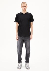 Zwarte crew neck t-shirt met korte mouwen, gecombineerd met donkergrijze jeans. Schoenen zijn lichtgrijs met accenten en hebben een mesh-ontwerp.