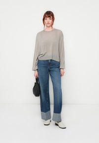 Lichtgrijze, lange mouw gebreide top in combinatie met wijdvallende blauwe jeans met een contrasterende denim manchet en witte enkellaarzen. Zwarte handtas.