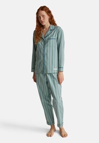 Svetle modrý pruhovaný pyžamový set vyrobený z měkké tkaniny; obsahuje košili na knoflíky s kapsou a kalhoty s manžetami a elastickým pasem.