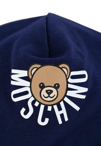Beanie in cotone blu navy con un viso di orso in stile cartoon e la scritta "Moschino" in bianco, con un motivo di maglia testurizzata.