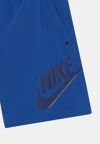 Niebieskie spodenki sportowe o gładkiej fakturze, z dużym ciemnoniebieskim logo Nike oraz guzikiem w pobliżu szwu kieszeni.