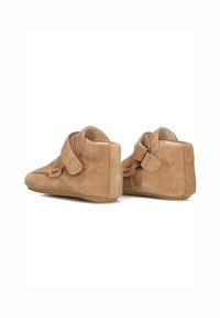 Beige suede enkellaarsjes met een klittenbandsluiting, ronde neus en een zachte textuur. Het ontwerp heeft een subtiele stiknaad en een iets verhoogde hak.