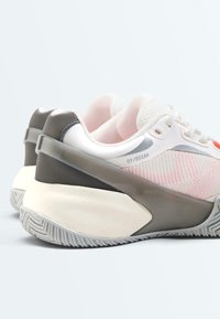 Paire de baskets de sport blanches et grises avec des côtés en mesh rose, des semelles épaisses et amortissantes, et une bride de soutien grise autour du talon.