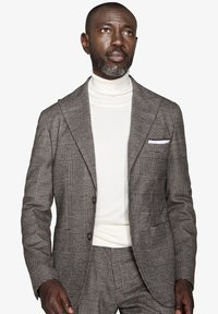 Gråternet blazer med spidse klapper, to knapper og et hvidt lommetørklæde, parret med en hvid polotrøje. Struktureret stof.