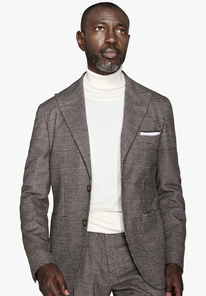 Gråternet blazer med spidse klapper, to knapper og et hvidt lommetørklæde, parret med en hvid polotrøje. Struktureret stof.
