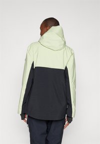 Giacca impermeabile con parte superiore verde menta e parte inferiore nera. Caratterizzata da un cappuccio, maniche lunghe e tasche laterali con zip. Tessuto liscio.