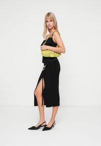 Rochie neagră ajustată, cu fenta laterală și accent din lanț argintiu. O geantă texturată de culoare verde lime, cu un închizător, asortată cu pantofi slingback negri.