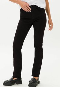 Jeans de mezclilla negra con un diseño ajustado, que cuentan con un cierre frontal de botón, bolsillos clásicos y una textura sutil. Combinados con mocasines negros gruesos.