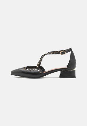 Chaussures à talons en cuir noir avec un design ouvert, bout pointu, bride à la cheville et accents en clous dorés. Elles disposent d'un petit talon carré.