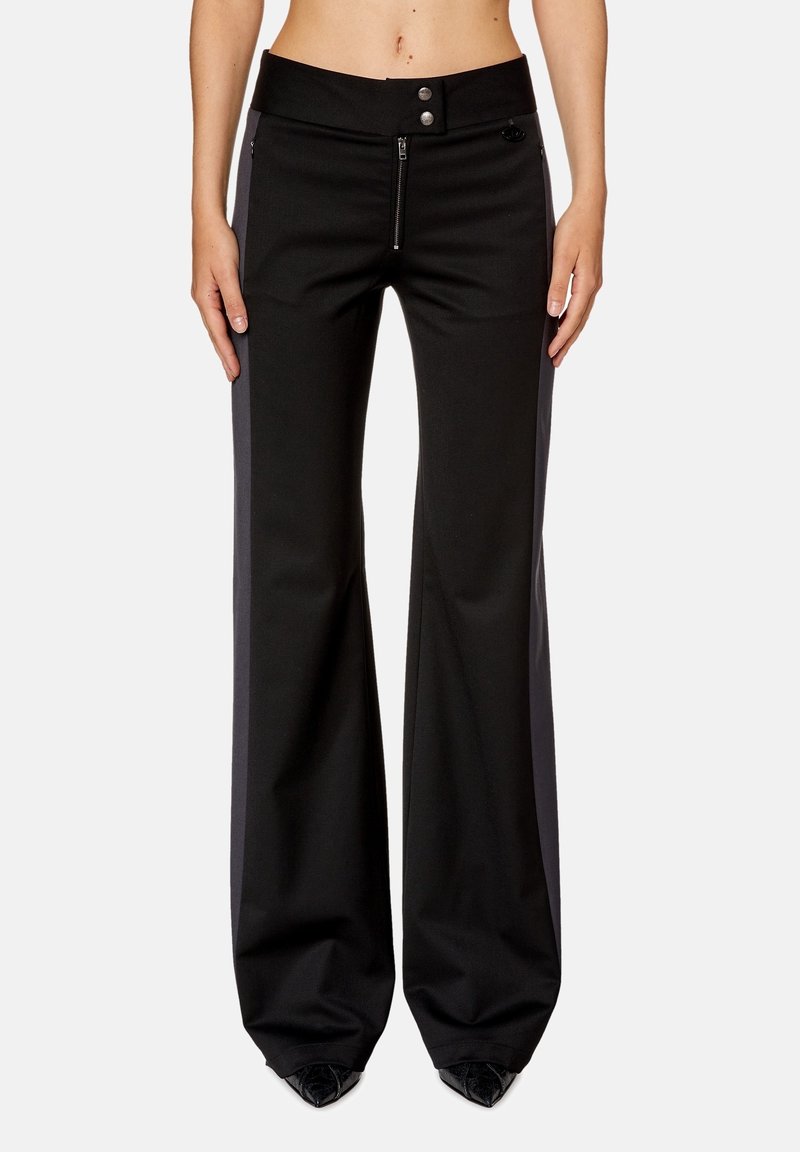 Pantalon noir à jambes larges avec fermeture éclair frontale et double bouton-pression, porté par une personne les mains relâchées le long du corps.