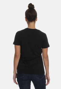 Czarna bawełniana koszulka z krótkim rękawem, standardowym okrągłym dekoltem i gładką teksturą, noszona z ciemnoniebieskimi dżinsami, pokazana od tyłu.