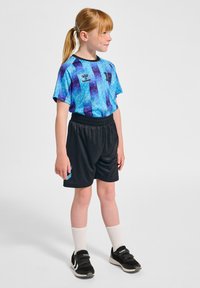 Blå och lila mönstrad sportskjorta, svarta shorts och svarta sneakers med kardborreband. Inkluderar vita strumpor och en logotyp på skjortan.