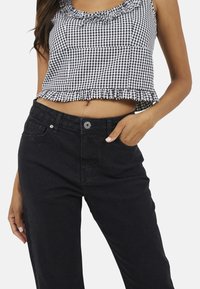 Jeans noirs cropped avec une taille haute et une poche. Assortis avec un haut sans manches en vichy noir et blanc, présentant un ourlet et un décolleté à volants.