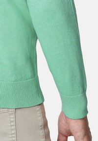 Suéter verde claro con ribetes en el dobladillo y los puños, hecho de un material de punto suave. Se muestra la manga, revelando una textura lisa.