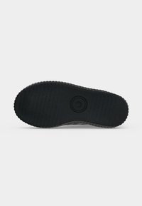Semelle de chaussure en caoutchouc noir avec une adhérence texturée et un logo circulaire au centre, vue depuis le dessous sur un fond neutre.