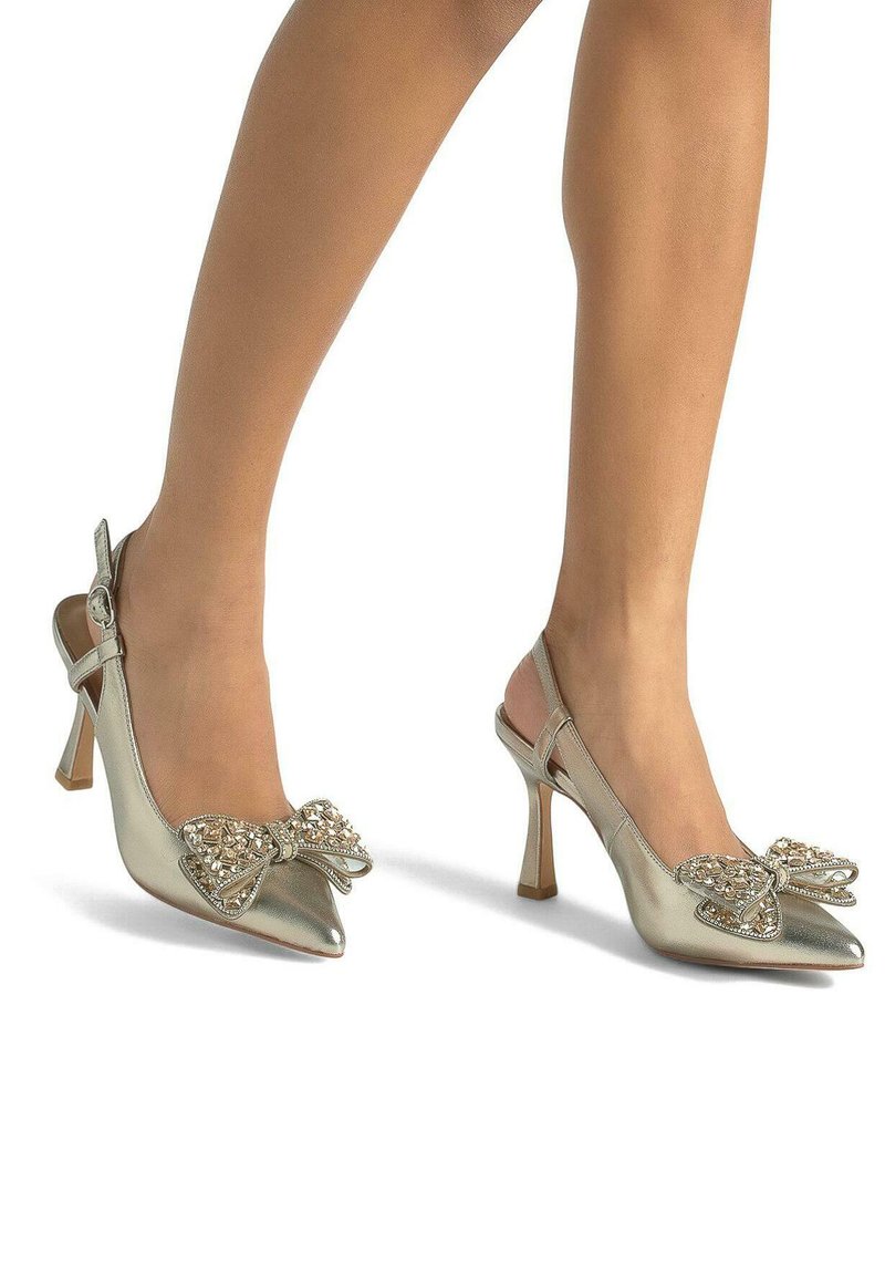Décolleté slingback argentate con punta affusolata, caratterizzate da un grande fiocco decorato con strass e un tacco alto e sottile. Texture metallica liscia.
