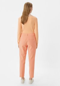 Lightweight, peach-colored sweater with long sleeves paired with tailored, pastel pink trousers. Both have a smooth texture and minimal detailing.