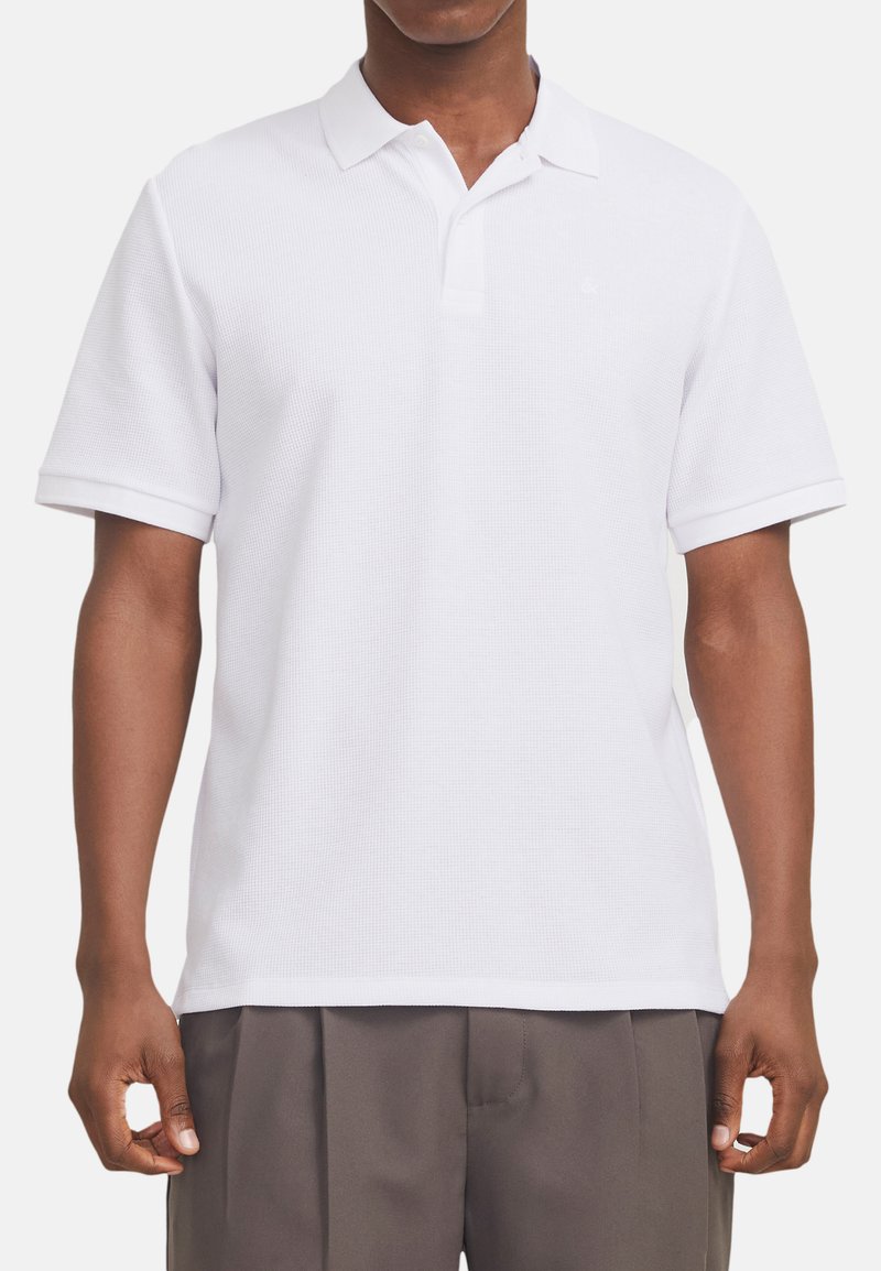 Polo blanc avec un tissu texturé, col et manches courtes. Présente un logo discret sur la poitrine et un ourlet droit.