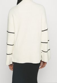 Vit ribbad tröja med hög hals, vida ärmar med svarta horisontella ränder och sidsprund för extra komfort.