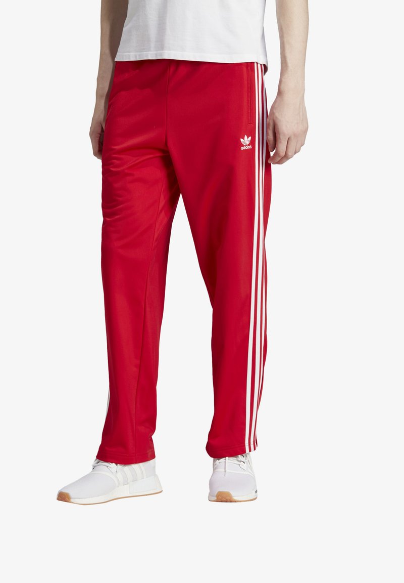 Rote Trainingshosen mit drei weißen Streifen an den Seiten. Hergestellt aus einem glatten, leichten Material und mit einem elastischen Bund.