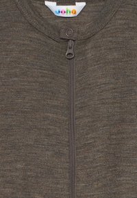 Brun zip-up plagg med ringdragkedja och rund krage, som visar en liten färgglad varumärkesskylt inuti halsområdet.
