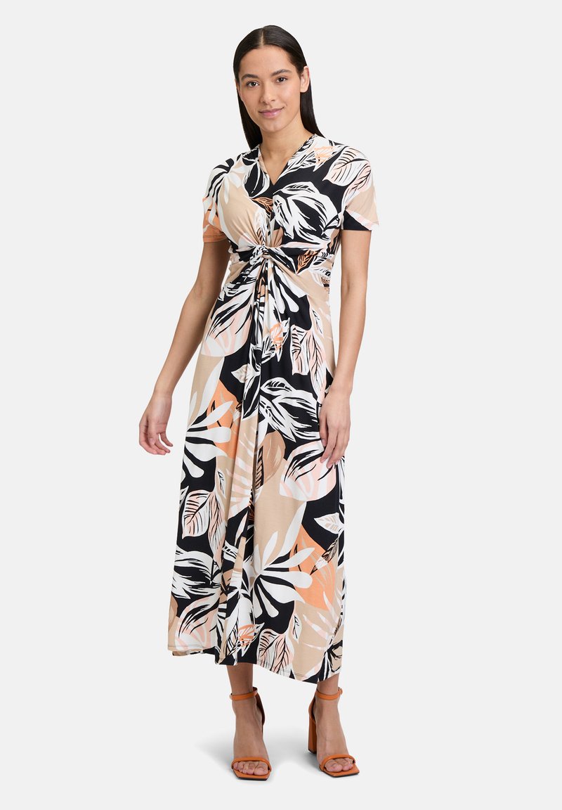 Maximekko, jossa on lyhyet hihat, vyötäröllä solmukohta, mustalla pohjalla suuria trooppisia lehtikuvioita persikassa, kermassa ja valkoisessa.