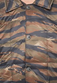 Camo pufferjack in bruin- en groentinten, met een drukknoopsluiting, gestikt ontwerp en een gladde, glanzende stof textuur.