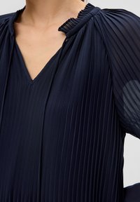 Navyblaues plissiertes Top mit V-Ausschnitt und gerafften Details am Kragen, mit halbtransparenten Ärmeln für zusätzliche Textur.