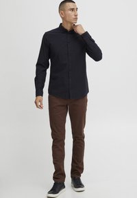 Sötét mintás, hosszú ujjú ing, gombos gallérral, barna, slim-fit nadrággal és fekete tornacipővel párosítva.