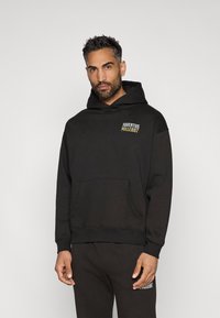 Mustast kapuutsiga sviiter, mis on valmistatud puuvilla segust, ees on tasku ja rinnas on print "JUVENTUS MILLE897." Lõtv lõige.