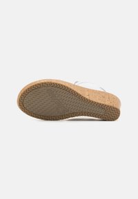 Sandal con tacco in sughero e suola in gomma testurizzata che mostra il logo Skechers, vista dal basso su uno sfondo bianco.