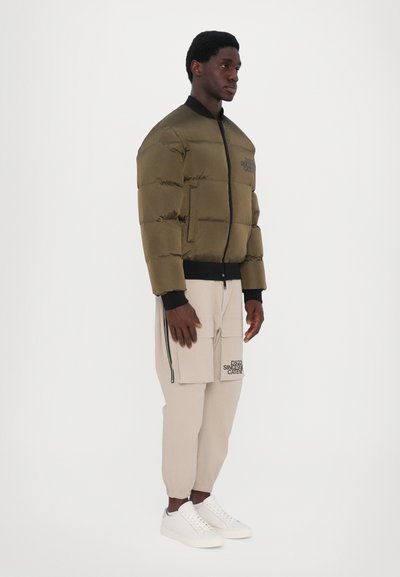 Doudoune verte olive avec un design matelassé, col côtelé noir et fermeture éclair à l'avant. Associée à un pantalon cargo beige et des baskets blanches.
