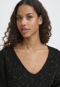 Black knitted sweater with a V-neck, featuring scattered silver sequins, soft texture, and a relaxed fit.