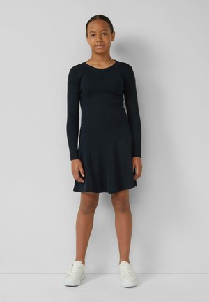 Schwarzes Langarmkleid mit rundem Ausschnitt, ausgestelltem Rock und weicher Textur, kombiniert mit weißen Sneakers. Einfaches und elegantes Design.