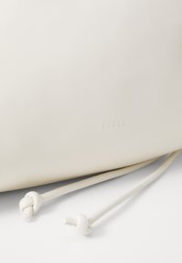Fehér bőr táska sima felülettel, húzózsinórral záródik, és dombornyomott "FURLA" márkázással rendelkezik. Egyszerű, minimalista dizájn.