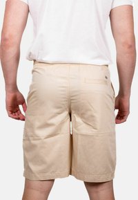 Pantaloni corti beige realizzati in tessuto leggero, con cintura elastica, tasche laterali e una singola tasca posteriore con un sottile logo decorativo.