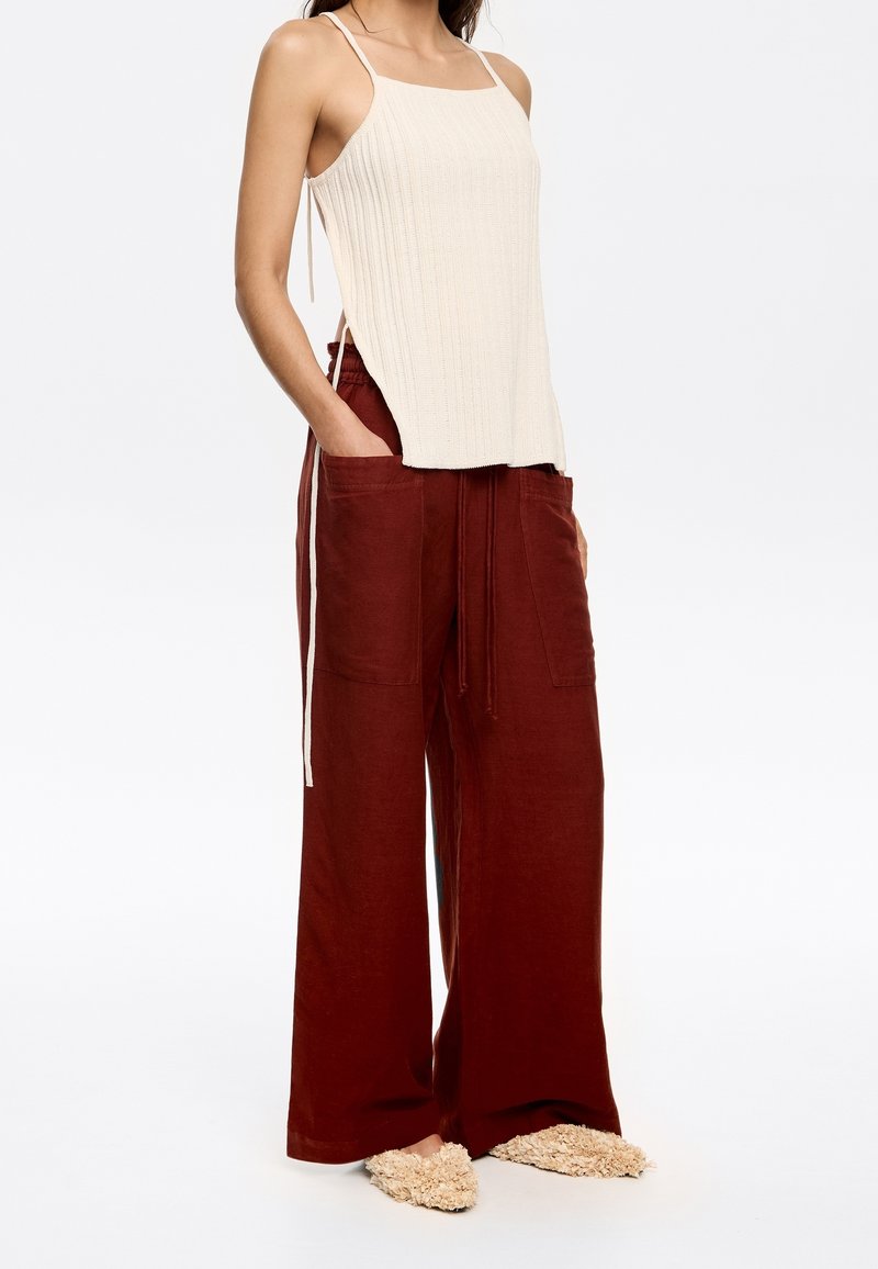 Light beige ribbed tank top with thin straps, paired with wide-leg rust-colored pants featuring front pockets and drawstring waistband.