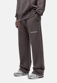 Dark gray sweatpants made of soft fabric, featuring side pockets and a small white print on the thigh. Paired with silver athletic shoes.