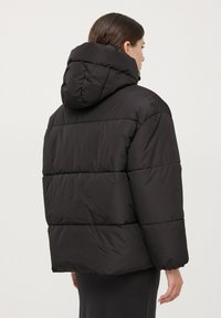 Giacca a vento nera con cappuccio, caratterizzata da un design trapuntato e una vestibilità rilassata. Il tessuto appare liscio con una leggera lucentezza.