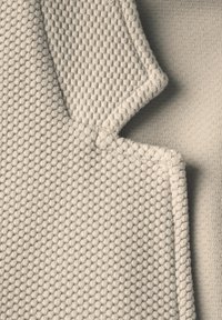 Beige textiel met textuur, voorzien van een geweven patroon aan de ene kant en een gladde afwerking aan de andere kant, met een afgeronde uitsparing en gestikte randen.