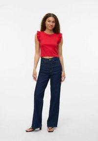 Rode katoenen crop top met gerimpelde mouwen, gecombineerd met hoge taille wijdvallende donkerblauwe denimjeans en zwarte slippers.