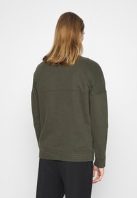 Sudadera verde con cuello redondo, mangas largas, puños y dobladillo acanalados. Textura suave con un diseño minimalista y sin logotipos visibles.