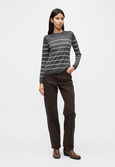 Γκρι ριγέ πουλόβερ με μακριά μανίκια και στρογγυλή λαιμόκοψη, συνδυασμένο με καφέ παντελόνια φαρδιάς γραμμής και καφέ μποτάκια αστραγάλου, σε απλό φόντο.