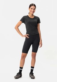 Fekete atlétikai póló és hozzáillő kerékpáros rövidnadrág légáteresztő anyagból, sötét kerékpáros cipővel és csíkos bokazoknival párosítva.