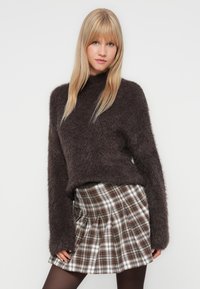 Bruine zachte trui met een hoge kraag, gecombineerd met een geplooide plaid minirok in wit, bruin en zwarte tinten.