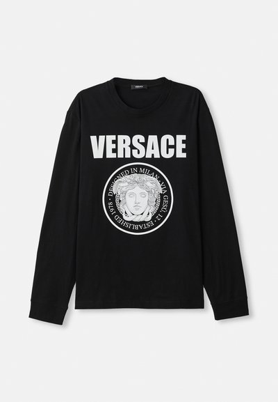 Fekete, hosszú ujjú póló, amelyen egy nagy fehér "VERSACE" logó és egy középső grafika látható, amely egy fej kör alakú mintában szerepel.
