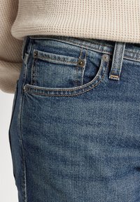 Jeans i medelblått denim med en lätt blekning, med stickade detaljer, framfickor och metallbeslag vid midjan.